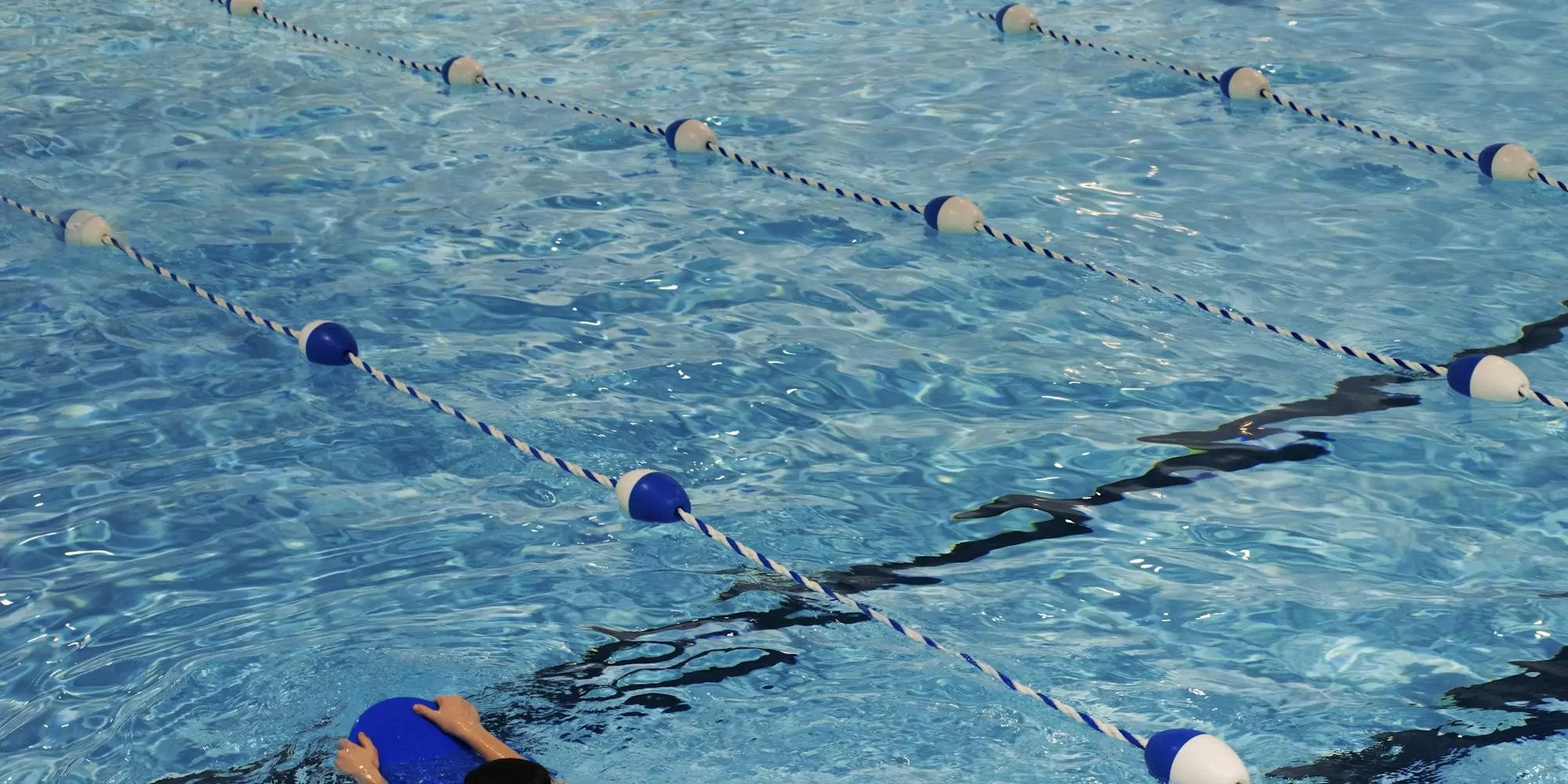 A young swimmer practicing with a kickboard in a swimming pool on a sunny day.