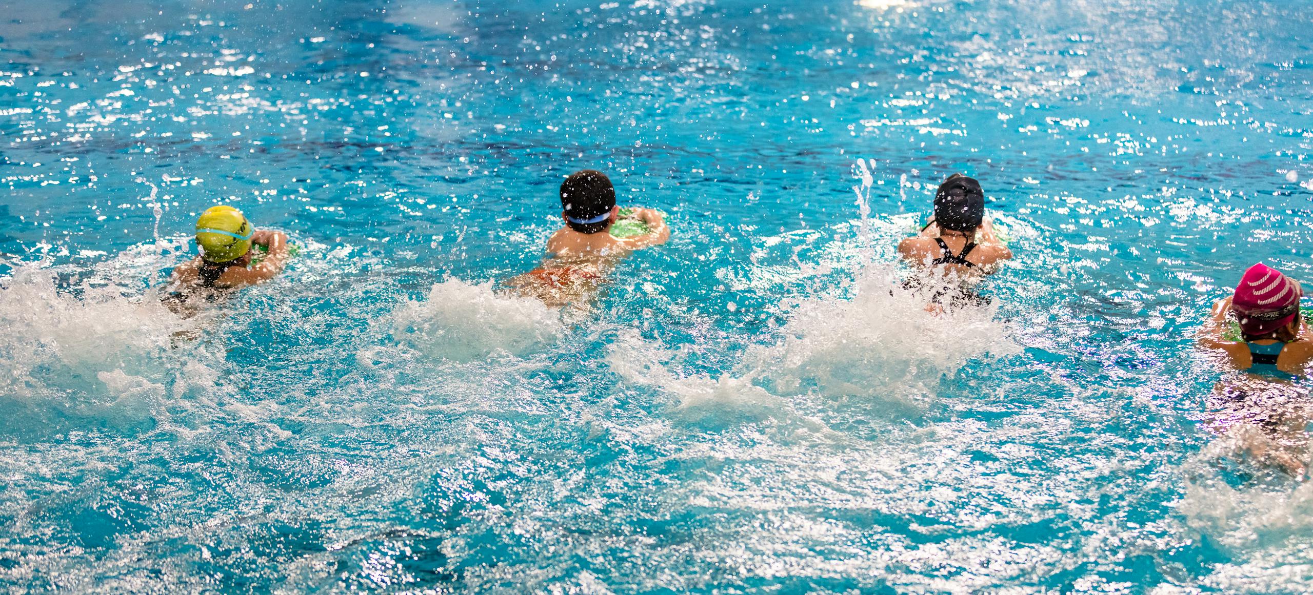 Group of children racing in an indoor swimming pool, making splashes.